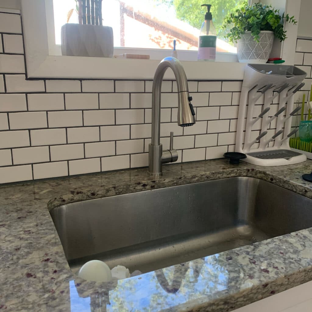 Stainless steel kitchen sink and pull-down faucet with white subway tile backsplash and countertop by window