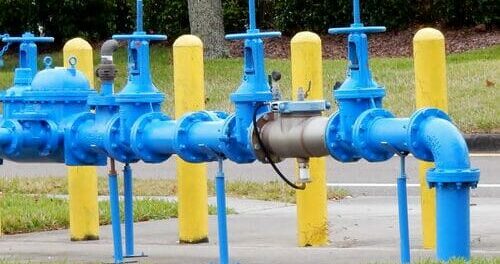 Blue backflow preventer valve assembly on water line with yellow bollards outside on a concrete pad