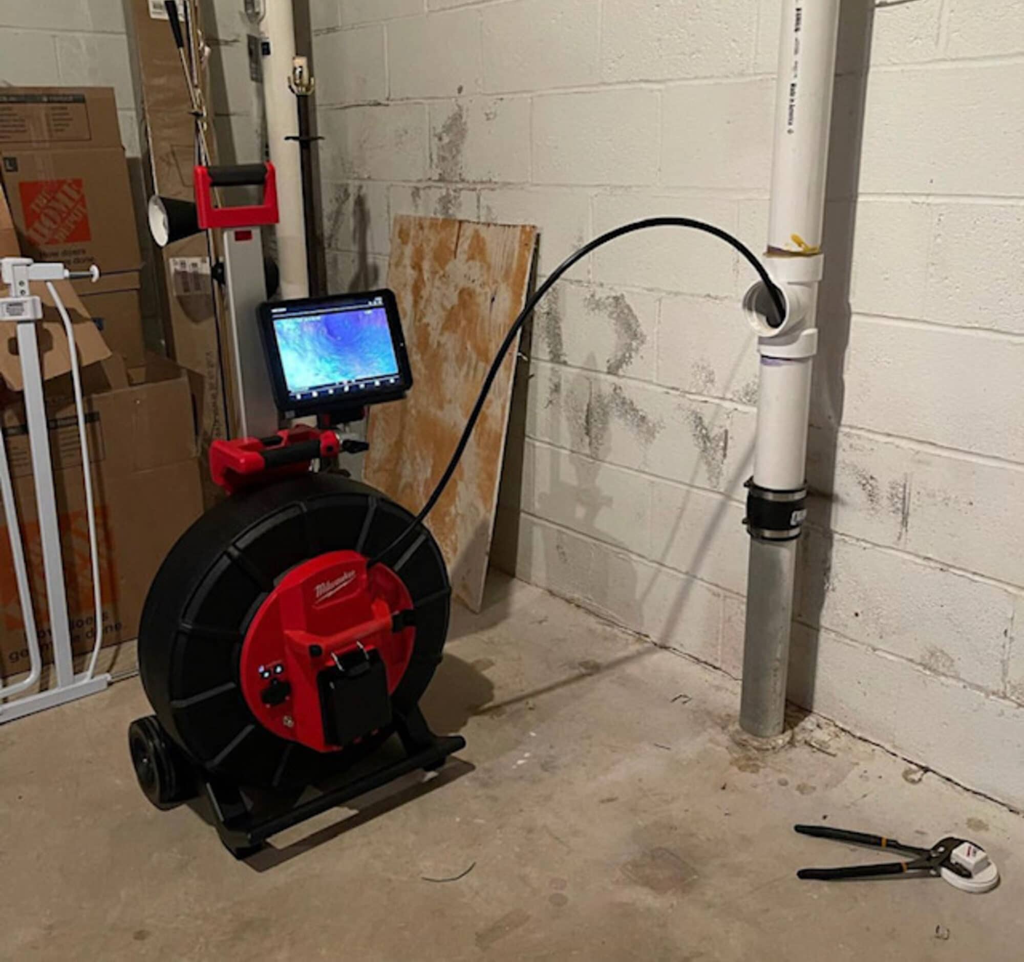 Sewer camera inspection equipment with monitor and cable reel connected to basement drain cleanout pipe