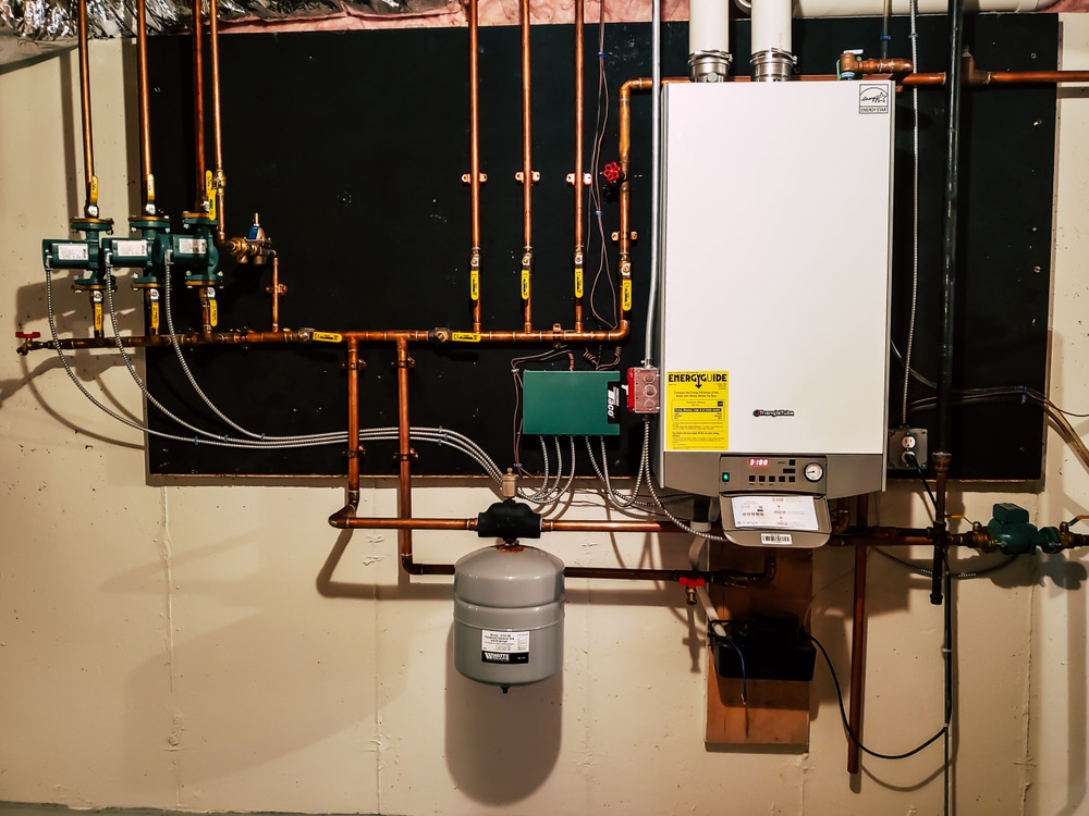 High-efficiency wall-mounted boiler with on-demand hot water system, copper piping, valves, and expansion tank in basement utility room