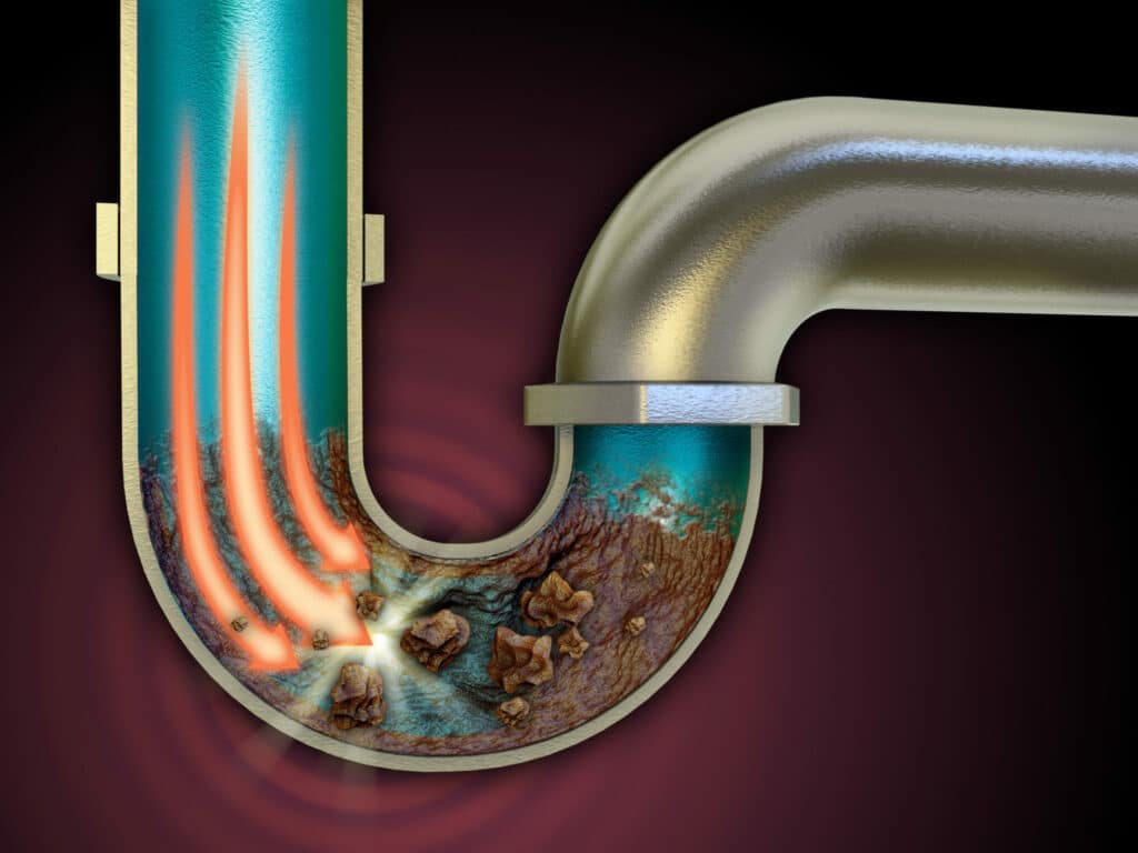 Cutaway of clogged U-shaped drain pipe with rust and debris buildup, showing hot water flushing through to clear blockage
