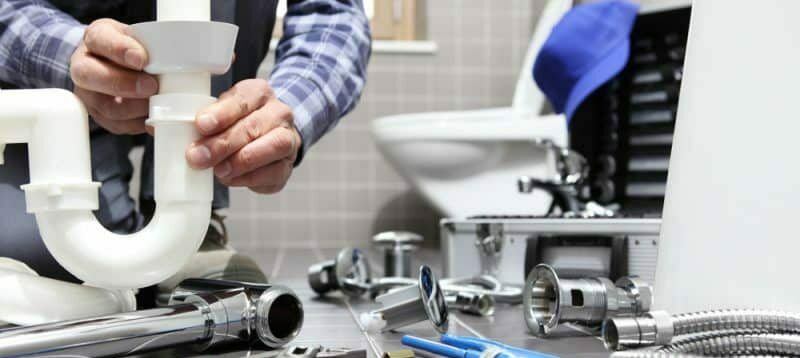 Plumber assembling white PVC P-trap under bathroom sink with chrome fittings and tools on countertop