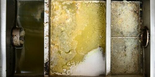Dirty sump pump basin with standing water, yellow sludge buildup, and foam residue on metal dividers