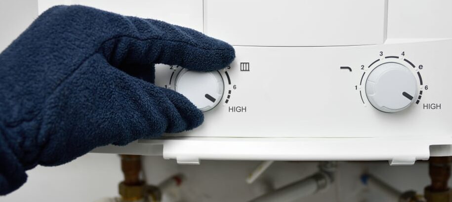 Gloved hand adjusting the temperature dial on a white tankless water heater control panel