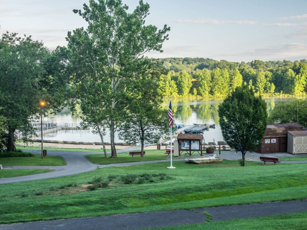 Lakeside view at Black Hill Regional Park with marina docks, trees, grassy hill, path, benches, and a flagpole near the shore