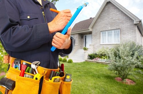 Plumber in uniform holding clipboard, tool belt with wrenches and tape measure, standing in front of a suburban house