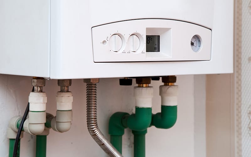 Wall-mounted tankless water heater with control dials and digital display, connected to plumbing pipes underneath