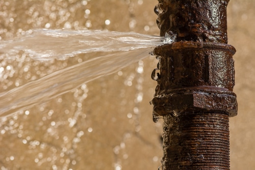Water spraying from leaking pipe joint, close-up of burst water line needing repair