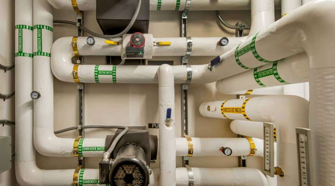Insulated commercial boiler room piping with labeled heating water and condenser lines, gauges, valves, and circulation pump