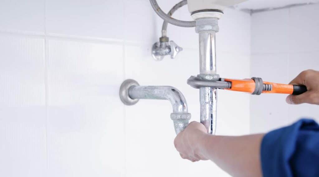 Plumber tightening sink drain pipe with a pipe wrench under a bathroom sink