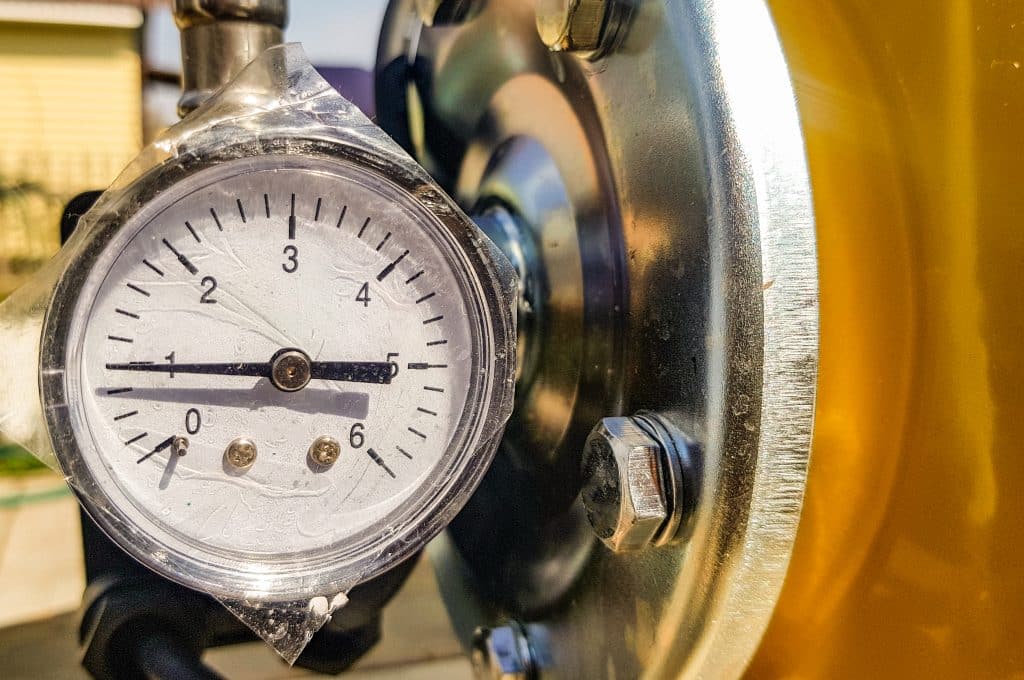 Close-up of a pressure gauge mounted on a metal pipe fitting, showing dial with scale from 0 to 6 on plumbing equipment