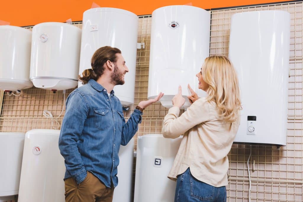 Smiling couple pointing at a wall-mounted boiler among several water heaters on display in a home appliance store