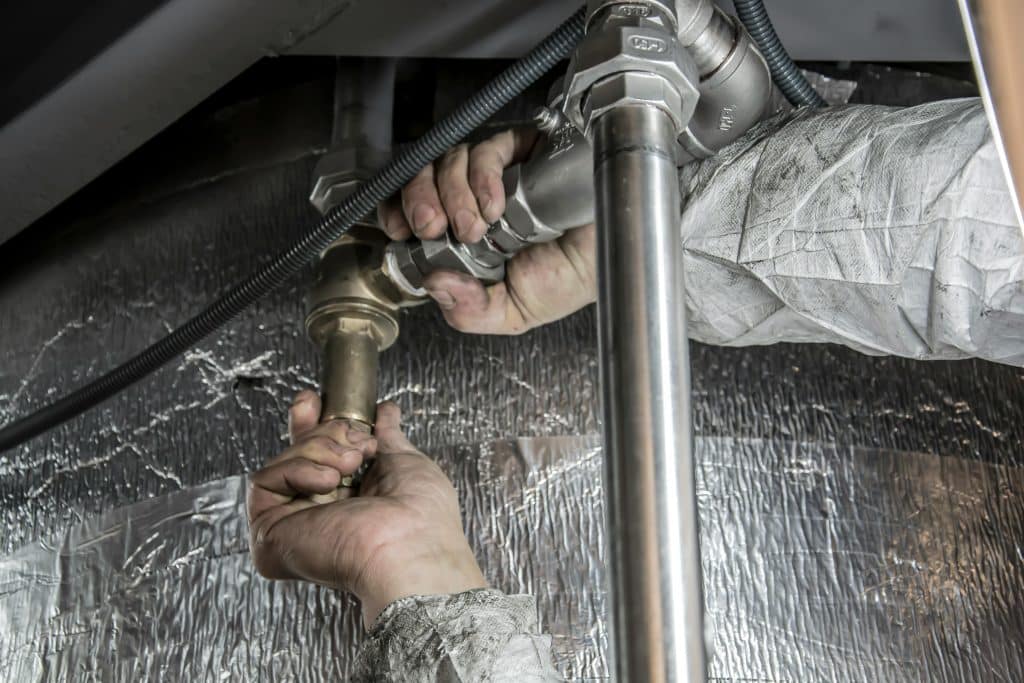 Hands tightening a pipe fitting on insulated plumbing under a ceiling during water leak repair