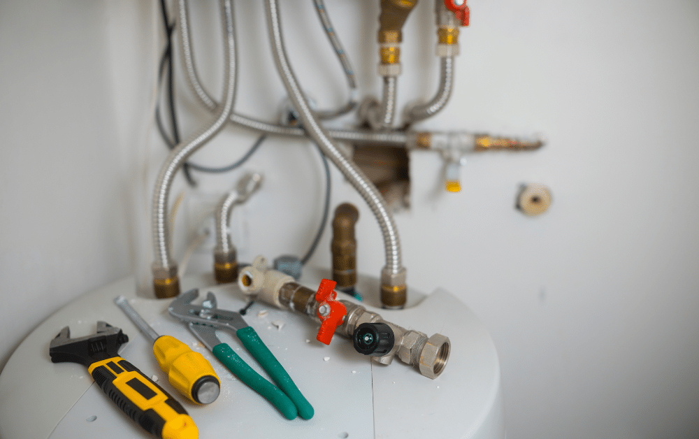 Plumbing repair tools and shutoff valve on a water heater, with braided hoses and pipe connections in the background